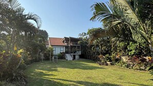 A residential property with a well-maintained lawn, a two-story house with a red roof, and surrounding tropical vegetation. - Sting-ray Cottage - Staynest Guesthouse (Port Edward)