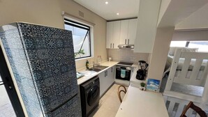 A compact kitchen with a washing machine, oven, and a dining area with a table and chairs. - Sting-ray Cottage - Staynest Guesthouse (Port Edward)