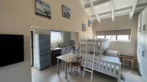 A compact living space with a kitchenette, a dining area, a bunk bed, and a television. - Sting-ray Cottage - Staynest Guesthouse (Port Edward)