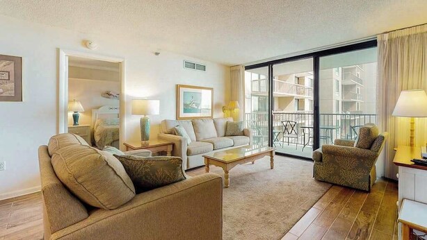 Ein Wohnzimmer mit einer Couch, Sesseln, einem Couchtisch und einem Balkon mit Gartenmöbeln.
