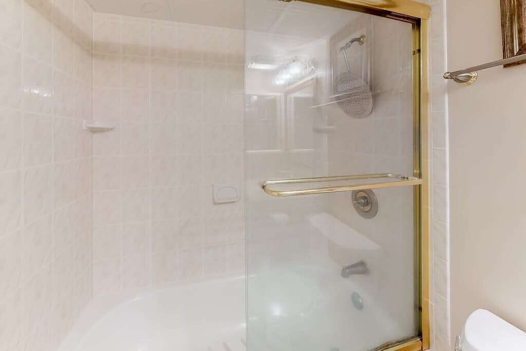 A glass-enclosed shower with a handrail, a visible showerhead, and a toilet in the adjacent room.