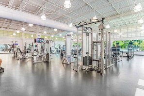 Ein großzügiger Fitnessraum mit verschiedenen Trainingsgeräten, einer hohen Decke mit Industrielicht und einem großen Fenster, das für natürliches Licht sorgt.