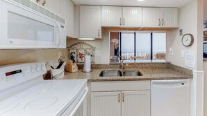 Una cocina con armarios blancos, microondas, estufa y lavavajillas.