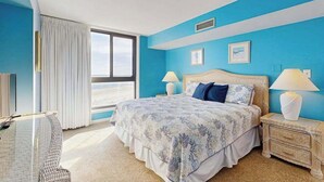 Une chambre avec un grand lit, deux tables de chevet avec des lampes, une fenêtre avec des rideaux et une vue sur le ciel.