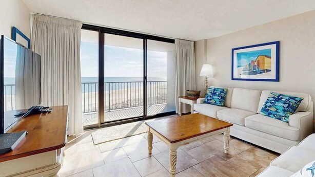 Une chambre d’hôtel avec un balcon, un canapé, une table basse, une télévision et un tableau au mur.