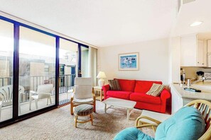 Ein Wohnzimmer mit einem roten Sofa, weißen Sesseln, einem Couchtisch und einem Balkon mit Glastüren.