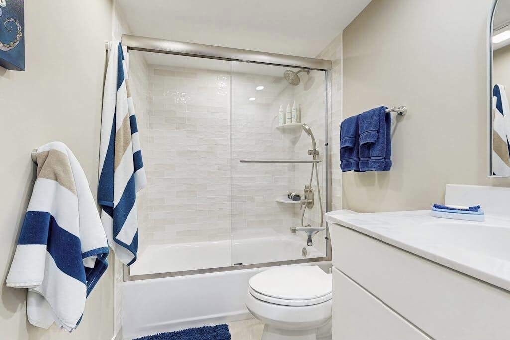 Un baño con ducha envuelta en vidrio, inodoro blanco y lavamanos con espejo.