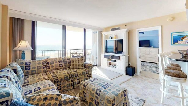 A living room with a sofa set, a TV, a dining area, and a view of the sea. - Sea Colony Ocean Fifth-Floor Condo with Hot Tub, Pool, & Basketball (Bethany Beach)