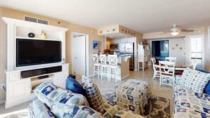 A living room with a flat-screen TV, a sofa, and a dining area with chairs and a table. - Sea Colony Ocean Fifth-Floor Condo with Hot Tub, Pool, & Basketball (Bethany Beach)