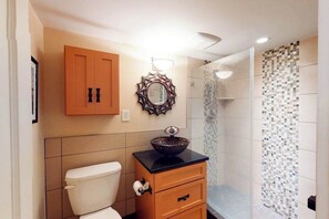 A bathroom with a toilet, a sink with a decorative bowl, a mirror with a unique frame, and a shower area with mosaic tiles. - Sea Colony 3rd floor condo w/ shared sauna, gym, pool & ocean view (Bethany Beach)