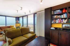 Ein modernes Wohnzimmer mit einer Couch, einem Couchtisch, einem Bücherregal und Meerblick durch große Fenster.