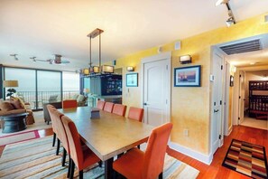 A modern dining area with a long table, orange chairs, and pendant lighting. - Sea Colony 3rd floor condo w/ shared sauna, gym, pool & ocean view (Bethany Beach)