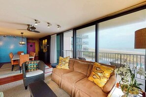 Ein modernes Wohnzimmer mit einer Couch, einem Esstisch und Stühlen. Es gibt einen Balkon mit Geländer und Blick ins Freie.