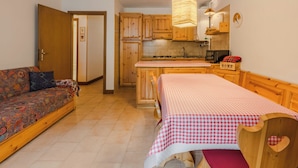 Un espacio habitable compacto con sofá, cama con ropa de cama a cuadros, zona de cocina con armarios de madera y una lámpara colgante.