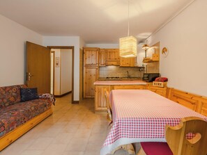 Ein gemütlicher Wohnraum mit Sofa, Bett mit karierter Bettwäsche, Küchenzeile mit Holzschränken und einer Pendelleuchte.