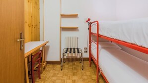Una habitación pequeña y funcional con una cama individual superpuesta, un escritorio y una silla.