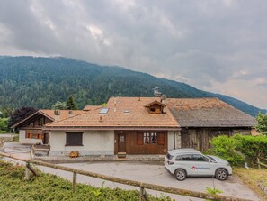 Ein rustikales Berggut mit Ziegeldach, einer Holztür und einem geparkten Auto davor.