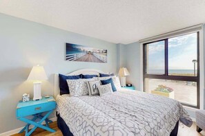 A bedroom with a bed, two bedside tables, a window with a view, and a painting on the wall. - Sea Colony Ocean 1st floor condo w/ tennis court, balcony, and pool (Bethany Beach)