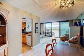 A spacious dining area with a wooden table and chairs, a kitchen with wooden cabinets, and a large sliding glass door leading to an outdoor patio. - Sea Colony Ocean 1st floor condo w/ pools, private beach and free WiFi (Bethany Beach)