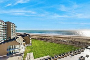 Un hotel frente a la playa con vista al océano, un área verde y un estacionamiento.