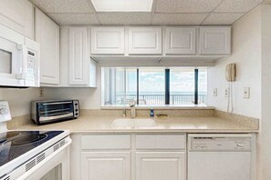 Una cocina con armarios blancos, microondas, tostadora, pileta y ventana con vista.