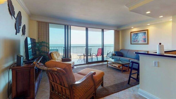 Een woonkamer met een bank, fauteuil en een kleine tafel. Er is een balkon met uitzicht op de oceaan.