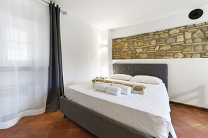 Una camera da letto con una parete in pietra, un letto con biancheria da letto bianca e una testiera grigia.