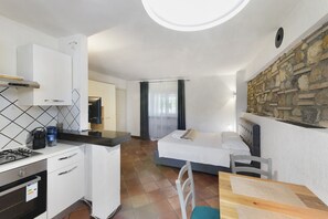 Una stanza funzionale con angolo cottura, un letto, una parete in pietra e una finestra con tende.