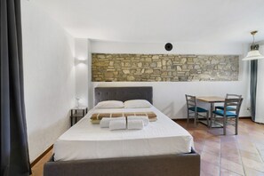 Una camera da letto con un letto, un muro in pietra, un tavolino e una sedia.