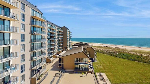 Ein mehrstöckiges Hotel mit Balkonen, Blick auf den Strand und einer Rasenfläche.