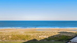 Blick auf einen Strand mit blauem Himmel, sandigem Ufer und grasbewachsenen Dünen.