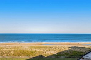 Blick auf einen Strand mit blauem Himmel, sandigem Ufer und grasbewachsenen Dünen.