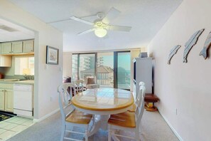 A dining area with a round table and chairs, a ceiling fan, and a view through a glass door to a balcony. - Sea Colony Ocean 3rd floor condo w/ pool, tennis court, and gym (Bethany Beach)