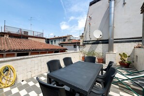 Una terraza en la azotea con una mesa, sillas, plantas en macetas y una manguera.