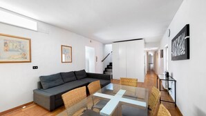 A modern living room with a glass-top dining table, grey sofa, wicker chairs, and artwork on the walls. - ‘Casa Dolce La Terrazza’ Apartment with Wi-Fi and Air Conditioning (Verona)