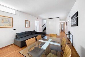 Una sala de estar moderna con una mesa de comedor de vidrio, sofá gris, sillas de mimbre y obras de arte en las paredes.