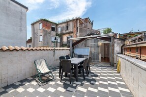 Une terrasse avec un sol à carreaux, une table entourée de chaises, un fauteuil de jardin à rayures et un espace clos par des parois de verre.