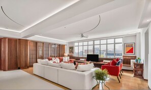A spacious living room with a white sofa, red chairs, a TV, and large windows offering a city view. - Kensington 6-bed 4000 Sqft AC Parking (London)