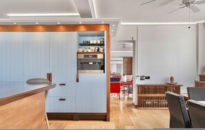 A modern kitchen with built-in appliances, a wooden counter, and a dining area with a red chair and wooden table. - Kensington 6-bed 4000 Sqft AC Parking (London)