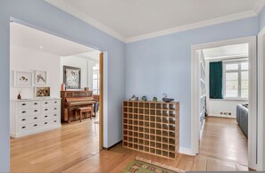 A room with a piano, a white cabinet, a wooden rack, and a view through a window. - Kensington 6-bed 4000 Sqft AC Parking (London)