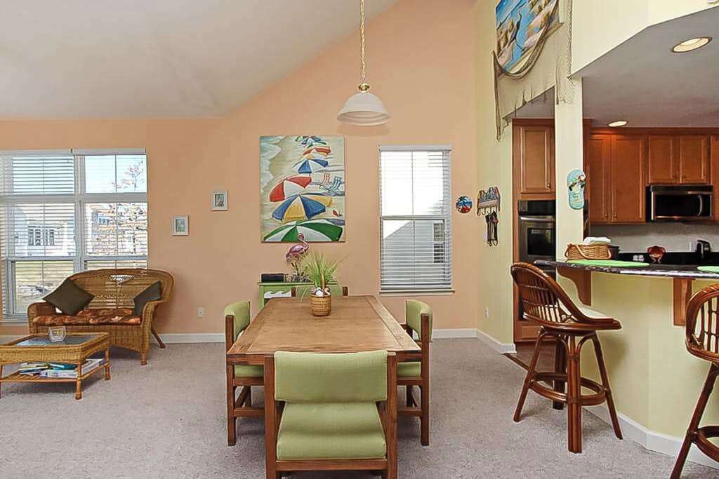 Een eetgedeelte met een houten tafel, groene fauteuils en een hanglamp.