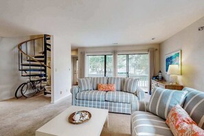 A living room with a sofa, a coffee table, a staircase, and a bicycle. - Sea Colony Tennis townhouse w/ free WiFi, tennis court, shared sauna, and pool (Bethany Beach)