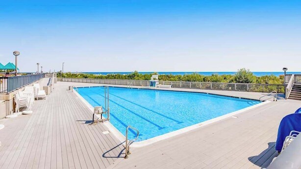 Une piscine avec une terrasse en bois, des chaises longues et une vue sur l’océan.