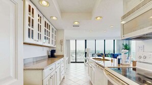 A modern kitchen with white cabinets, a built-in oven, and a large window overlooking a balcony. - Sea Colony 6th floor condo w/ balcony, shared tennis court & partial ocean view (Bethany Beach)