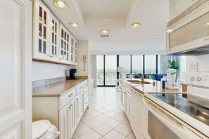 Een moderne keuken met witte kasten, een ingebouwde oven en een groot raam met uitzicht op een balkon.
