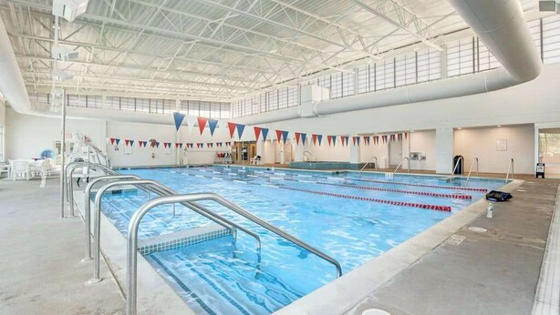 An indoor swimming pool with clear lanes, metal railings, and a high ceiling with visible structural beams. - Sea Colony 6th floor condo w/ balcony, shared tennis court & partial ocean view (Bethany Beach)