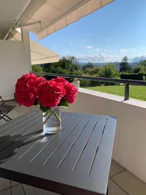 Un balcón con una mesa, un jarrón de flores y vistas a zonas verdes y montañas.