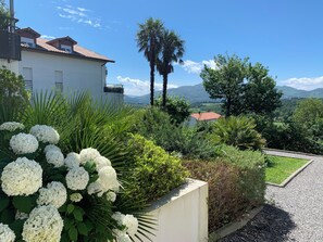 Zona residencial com um edifício branco, vegetação exuberante e vista clara para montanhas distantes.