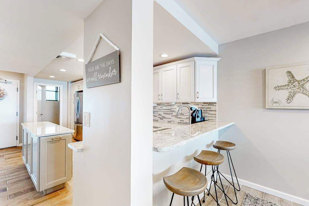 A kitchen with white cabinets, a marble countertop, and a bar area with stools.