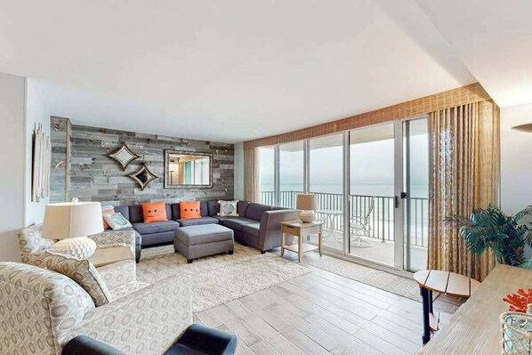 A spacious living room with a large sofa set, a coffee table, and a dining area. There is a balcony with a view of the ocean. - Sea Colony Ocean 14th floor condo with elevator, WiFi, and basketball court (Bethany Beach)